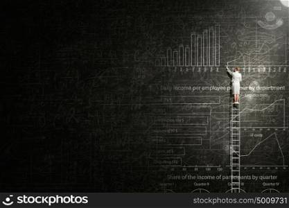 Financial education. Back view of businesswoman standing on ladder and drawing sketch on wall