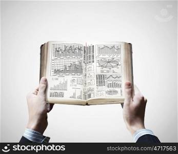 Financial education. Close up of male hands holding opened book with sketches