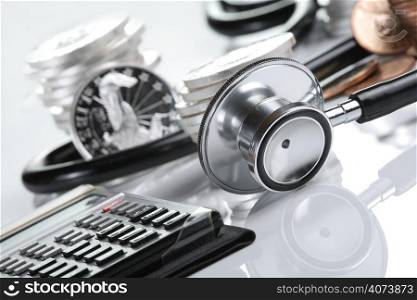 Financial health concept, stethoscope weaving around stacks of silver and gold coins and calculator
