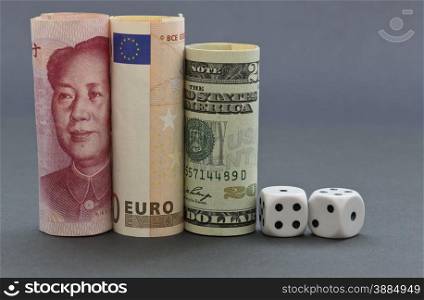 Financial investment risks reflected in dice next to dollar, euro, and yuan money on gray and blue hued background. Three currencies build concept of global marketplace and shared gambles.