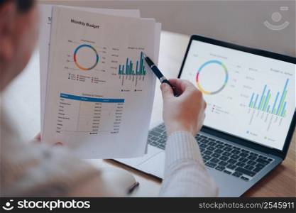 Financial round diagram on laptop screen and on paper. Man is doing paperwork, occupied with sells through internet. Online trading. Display of PC and phone on the desk. Monthly budget planning.. Financial round diagram on laptop screen and on paper. Man doing paperwork. Monthly budget planning.