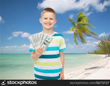 financial, summer, childhood and travel concept - smiling boy holding dollar cash money in his hand over tropical beach background