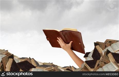 Find your book. Hand with book reaching out from pile of old books