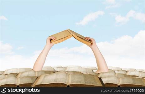 Find your book. Hand with book reaching out from pile of old books