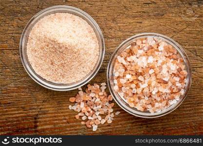 fine and coarse crystals of pink Himalayan salt in glass bowls on rustic wood, top view