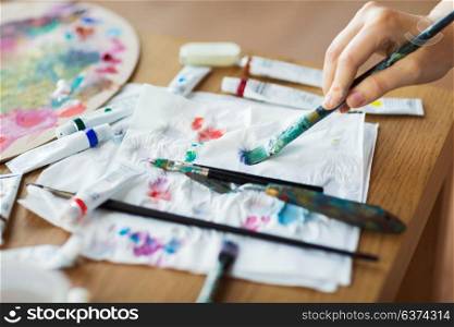 fine art, creativity and artistic tools concept - artist hand drying paintbrush with paper tissue. artist hand with paintbrush, paper and paint tubes
