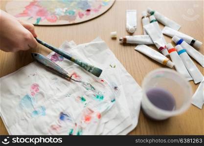 fine art, creativity and artistic tools concept - artist hand with paintbrush, palette knife, paper tissue and paint tubes. artist hand with paintbrush, paper and paint tubes