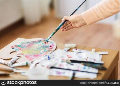 fine art, creativity and artistic tools concept - artist hand with paintbrush, and palette painting at studio. artist hand with paintbrush and color palette
