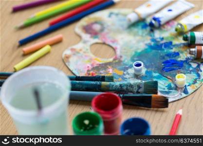 fine art, creativity and artistic tools concept - close up of palette, brushes, paint tubes and gouache colors on table. palette, brushes and paint tubes on table