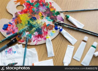 fine art, creativity and artistic tools concept - close up of palette, brushes and paint tubes on table. palette, brushes and paint tubes on table