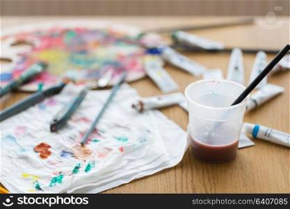fine art, creativity and artistic tools concept - paintbrush soaking in cup of water and color on paper tissue. paintbrush soaking in cup of water on table