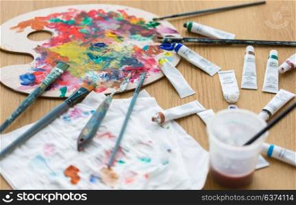 fine art, creativity and artistic tools concept - palette, brushes and paint tubes on table. palette, brushes and paint tubes on table