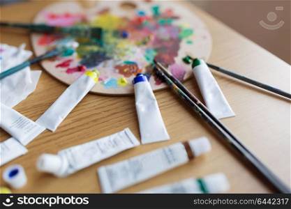 fine art, creativity and artistic tools concept - palette, brushes and paint tubes on table. palette, brushes and paint tubes on table
