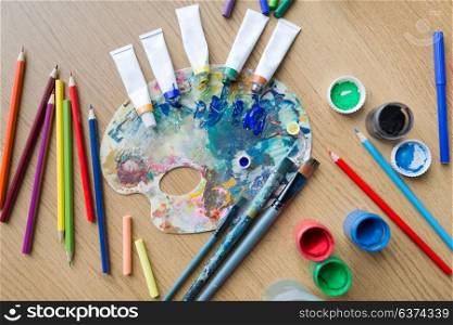 fine art, creativity and artistic tools concept - palette, brushes, paint tubes and gouache colors on table. color palette, brushes and paint tubes on table