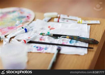 fine art, creativity and artistic tools concept - palette knife, brushes, paint tubes and paper tissue on table. palette knife, brushes and paint on paper tissue