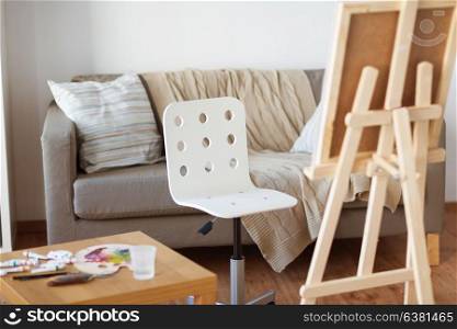 fine art, creativity and artistic tools concept - wooden easel and chair at home room or studio. wooden easel and chair at home room or art studio