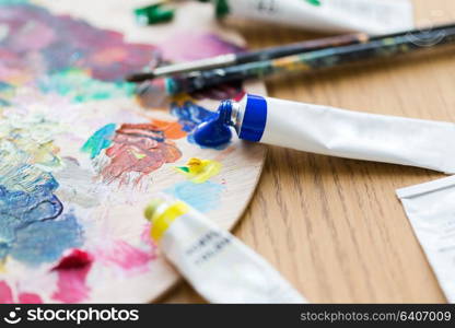 fine art, creativity, painting and artistic tools concept - close up of acrylic color or paint tubes, palette and brushes. acrylic color or paint tubes and palette