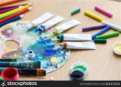 fine art, creativity, painting and artistic tools concept - close up of acrylic color or paint tubes with crayons and palette. acrylic color or paint tubes and palette