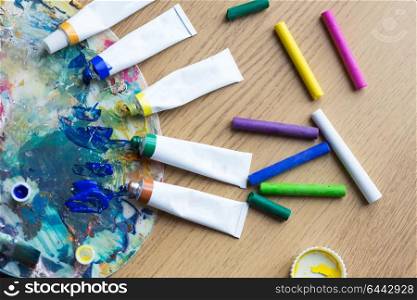 fine art, creativity, painting and artistic tools concept - close up of acrylic color or paint tubes with crayons and palette. acrylic color or paint tubes and palette