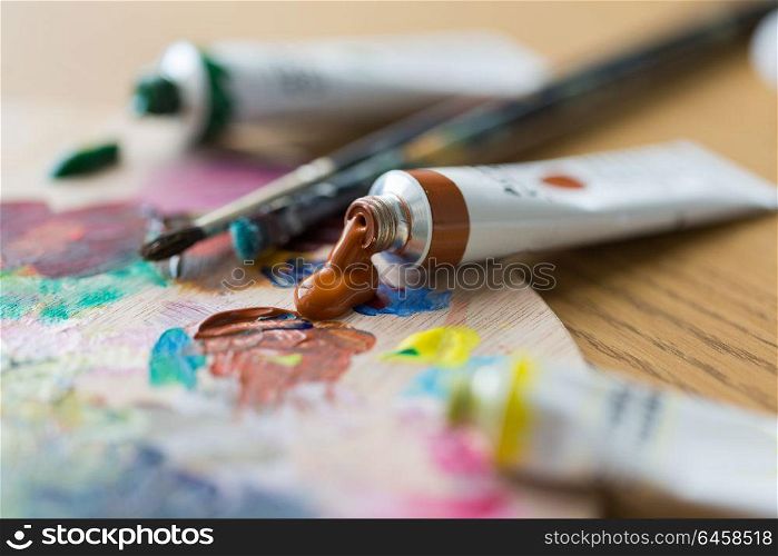 fine art, creativity, painting and artistic tools concept - close up of acrylic color or paint tubes, palette and brushes. acrylic color or paint tubes and palette
