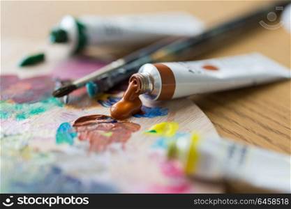 fine art, creativity, painting and artistic tools concept - close up of acrylic color or paint tubes, palette and brushes. acrylic color or paint tubes and palette
