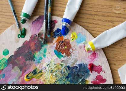 fine art, creativity, painting and artistic tools concept - close up of acrylic color or paint tubes, palette and brushes. acrylic color or paint tubes and palette. acrylic color or paint tubes and palette