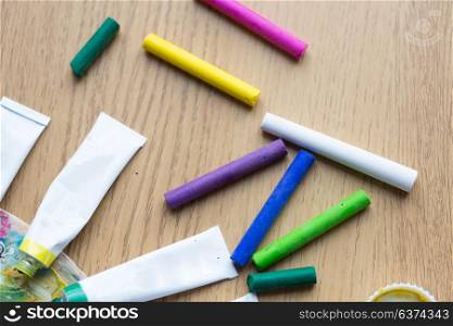 fine art, creativity, painting and artistic tools concept - crayons and acrylic color or paint tubes with palette on wooden table. crayons and acrylic color or paint tubes on table