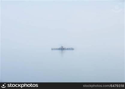Fine art minimalist image of derelict pier remains at sea during. Fine art minimalist landscape image of derelict pier remains at sea during foggy morning giving appearance of ruins floating
