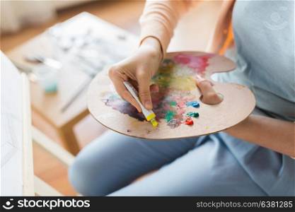 fine art, painting, creativity and people concept - close up of artist hand applying color paint to palette at studio. artist applying paint to palette at art studio