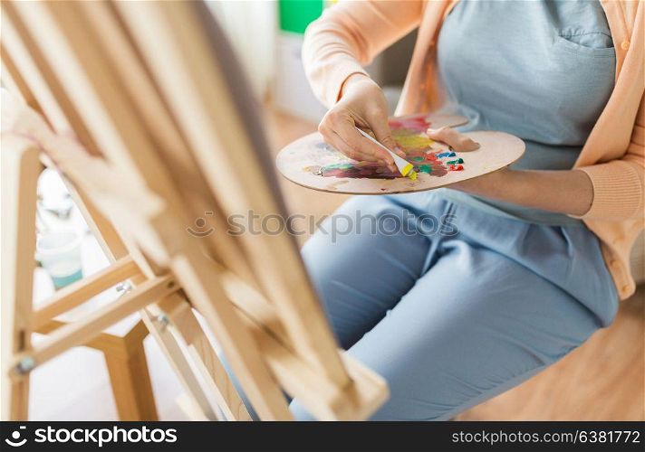 fine art, painting, creativity and people concept - close up of artist woman applying color paint to palette at studio. artist applying paint to palette at art studio