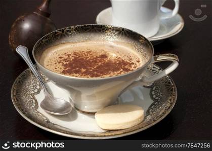 Fine porcelain cup with coffee, milk and sprinkled cinnamon on dark background