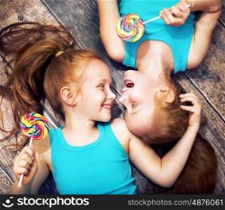 Fine portrait of a twin sisters holding colorful lollipops