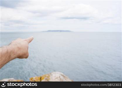 Finger pointing an island at the horizon on the sea