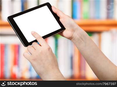 finger touches tablet pc with cut out screen on front of book shelves