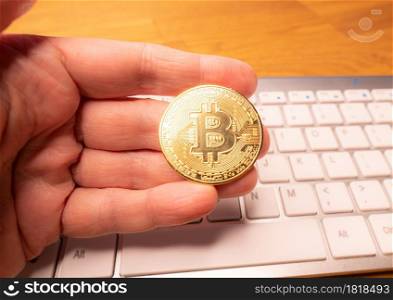 Fingers hold a gold bitcoin on the keyboard background