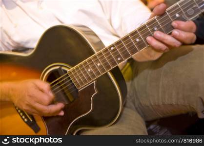 Fingers in motion on on the soundboard of an acoustic guitar