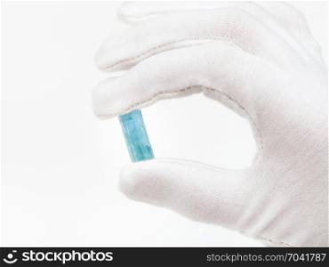 fingers in white glove holds aquamarine crystal close up on white background