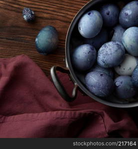 Finished blue-painted eggs in a copper pot with a burgundy apron on a wooden brown background. Stage of painting and cooking Easter eggs, preparing for the holiday, flat lay. copper pan with eggs and wooden spoon on old wooden background with apron