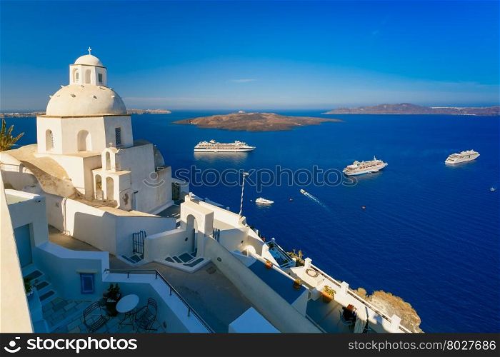 Fira, modern capital of the Greek Aegean island, Santorini, with orthodox church, cruise ships, caldera and volcano, Greece