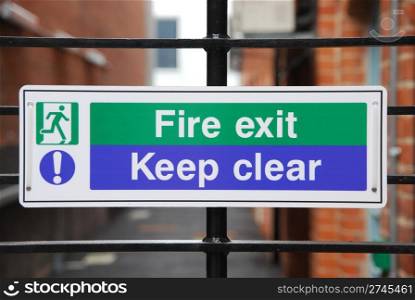 fire exit, keep clear sign hanging on a metallic fence
