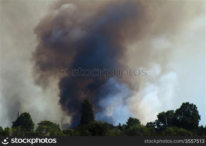 Fire in a field and thick clouds of smoke in the sky.