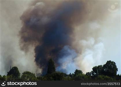 Fire in a field and thick clouds of smoke in the sky.