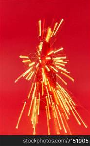 Firecracker from shined trails of Christmas lights on a painted wine bottle on a red background with copy space. New Year congratulation card.. Shined trails of Christmas garland lights as a firework.