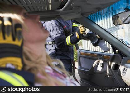 Firefighter cutting out a windshield after an accident with injured woman in foreground (selective focus)