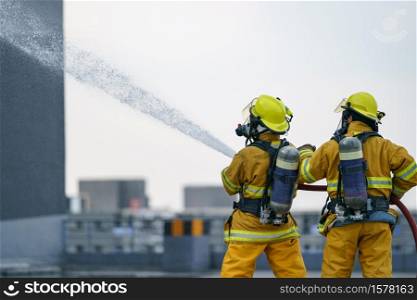 Firefighter or fireman team work water spray by high pressure nozzle to fire.