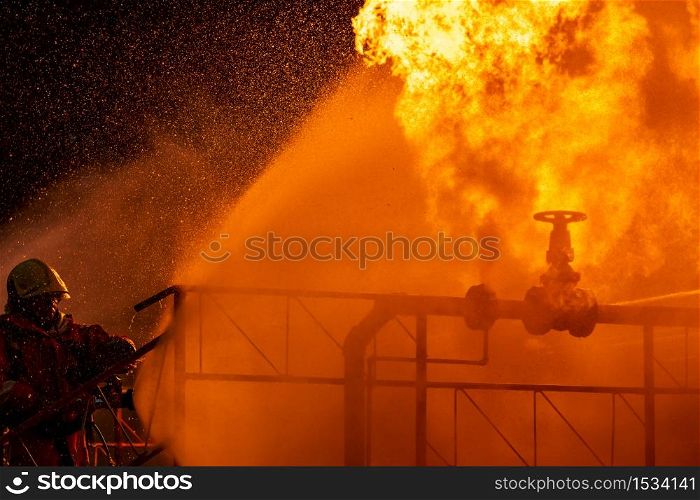 Firefighter using water fog type fire extinguisher to fighting with the fire flame from oil pipeline leak and explosion on oil rig and natural gas station. Firefighter and industrial safety concept.