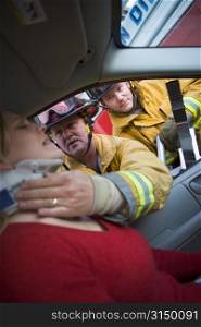 Fireman helping woman with neck brace while another fireman uses the jaws of life on a car door (selective focus)