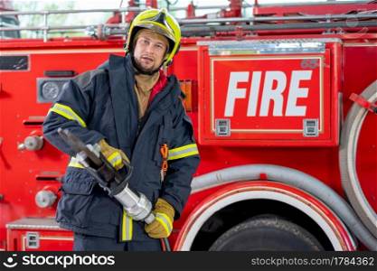 Fireman hold to for spreader tools and stand in front of fire truck. Concept of firefighter help people in emergency events.