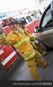 Fireman motioning for backup with another fireman using the jaws of life on a car door (blur)