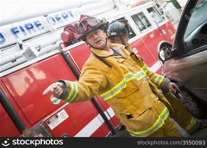 Fireman pointing at something with another fireman using the jaws of life on a car door